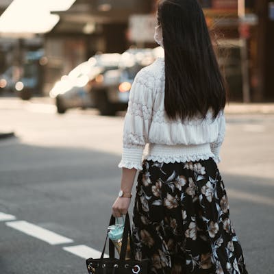 A woman in a floral skirt and white blouse walks down the street, surrounded by urban scenery.