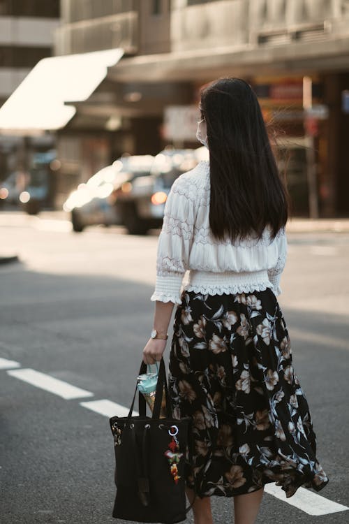 Free Woman in White Long Sleeve Shirt and Black Floral Skirt Standing on Sidewalk Stock Photo