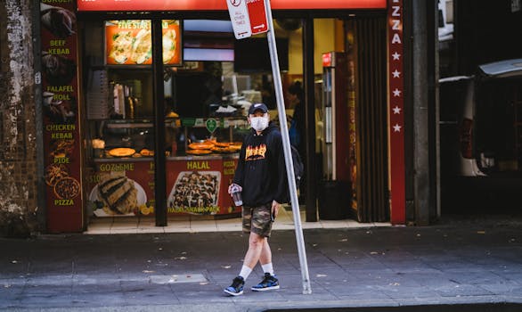 A man wearing a mask stands near a kebab shop on a Sydney sidewalk, reflecting urban life.