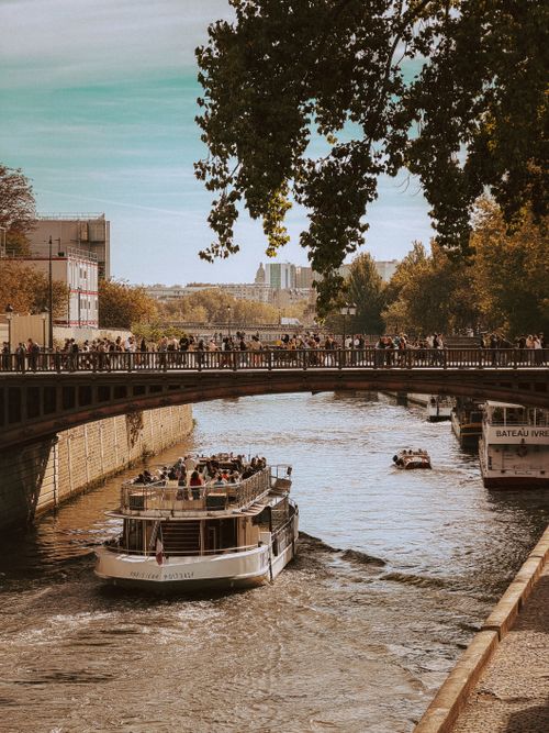 Free Charming view of the Seine River with a boat and a Parisian bridge bustling with people. Stock Photo