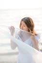 这是一张宁静的照片，照片中一位穿着白色连衣裙的女子在海边拥抱夏日微风