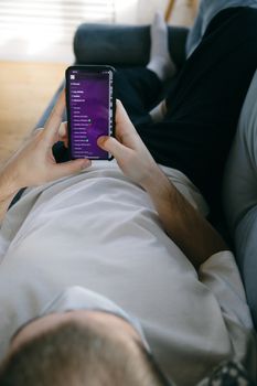 A man comfortably reclines on a sofa using a smartphone indoors, capturing a moment of leisure and connectivity.