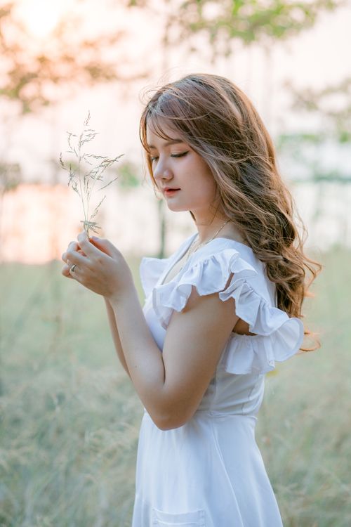 Free A peaceful portrait of a woman in a white dress, enjoying nature in a sunlit meadow. Stock Photo