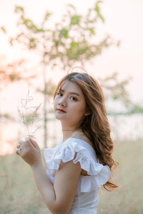 Free An Asian woman poses gracefully in a white dress outdoors, embodying summer elegance. Stock Photo