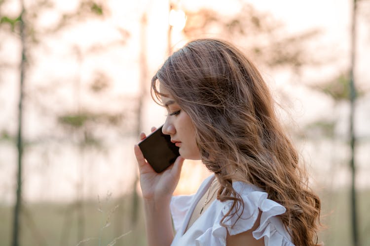 Young Woman Talking On Smartphone Standing In Forest