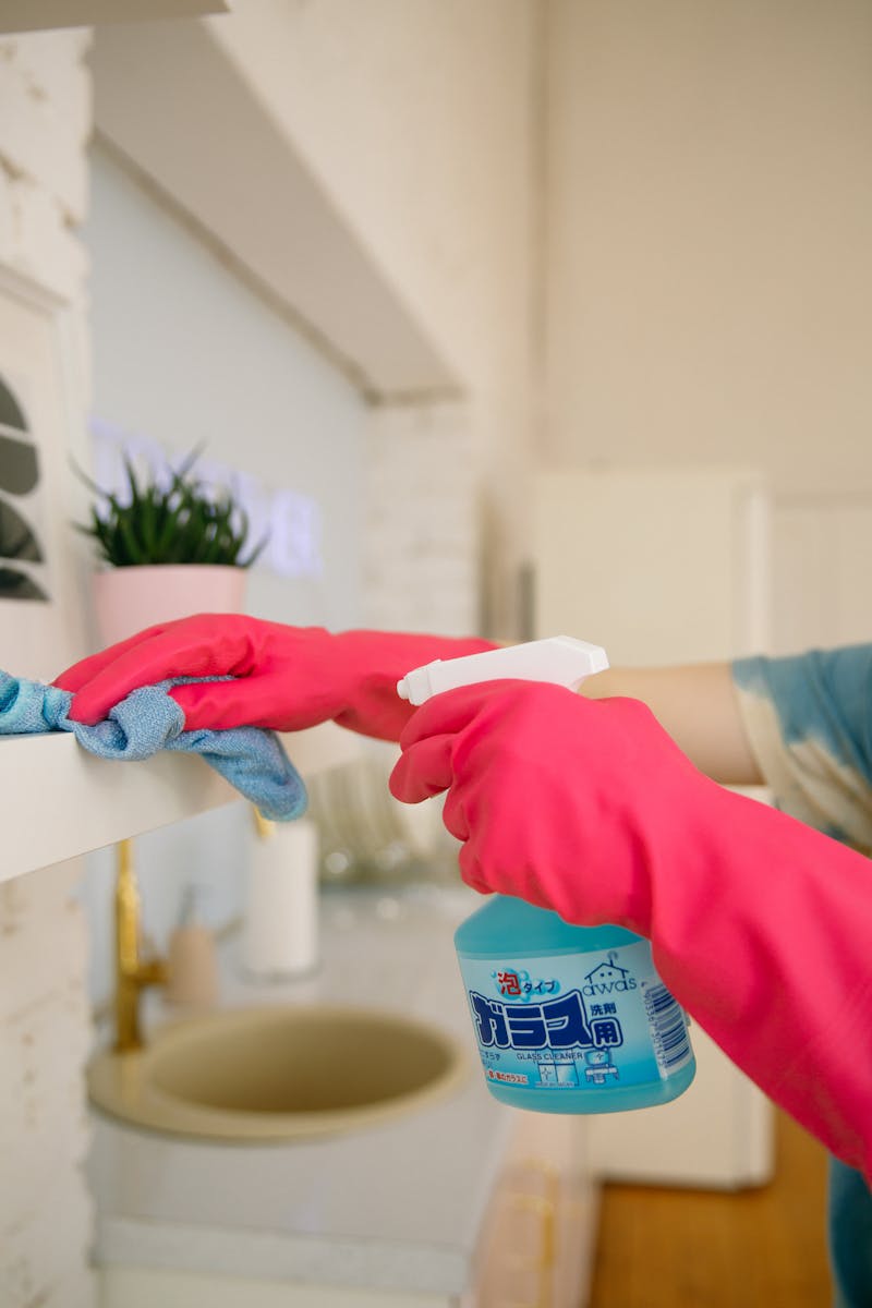 Close-up of person spraying disinfectant and wiping a home surface with a cleaning cloth