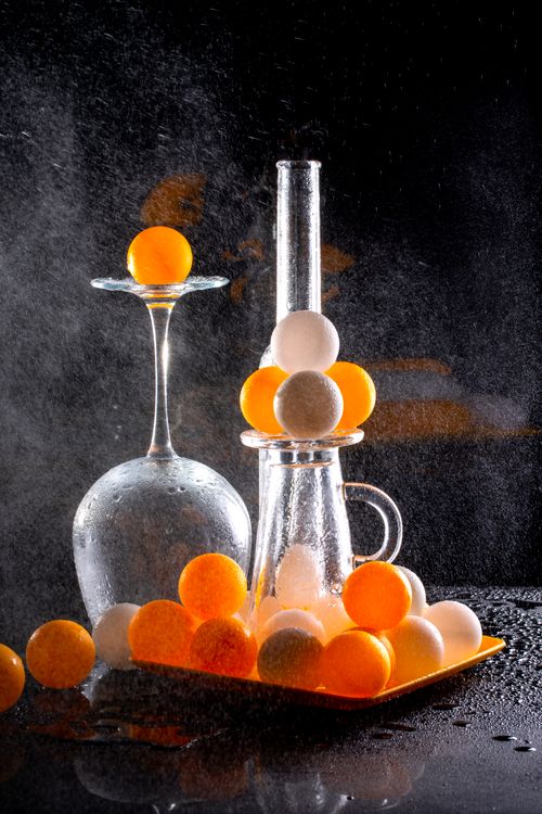 Free Artistic arrangement of orange and white ping pong balls with glassware in a dramatic light. Stock Photo