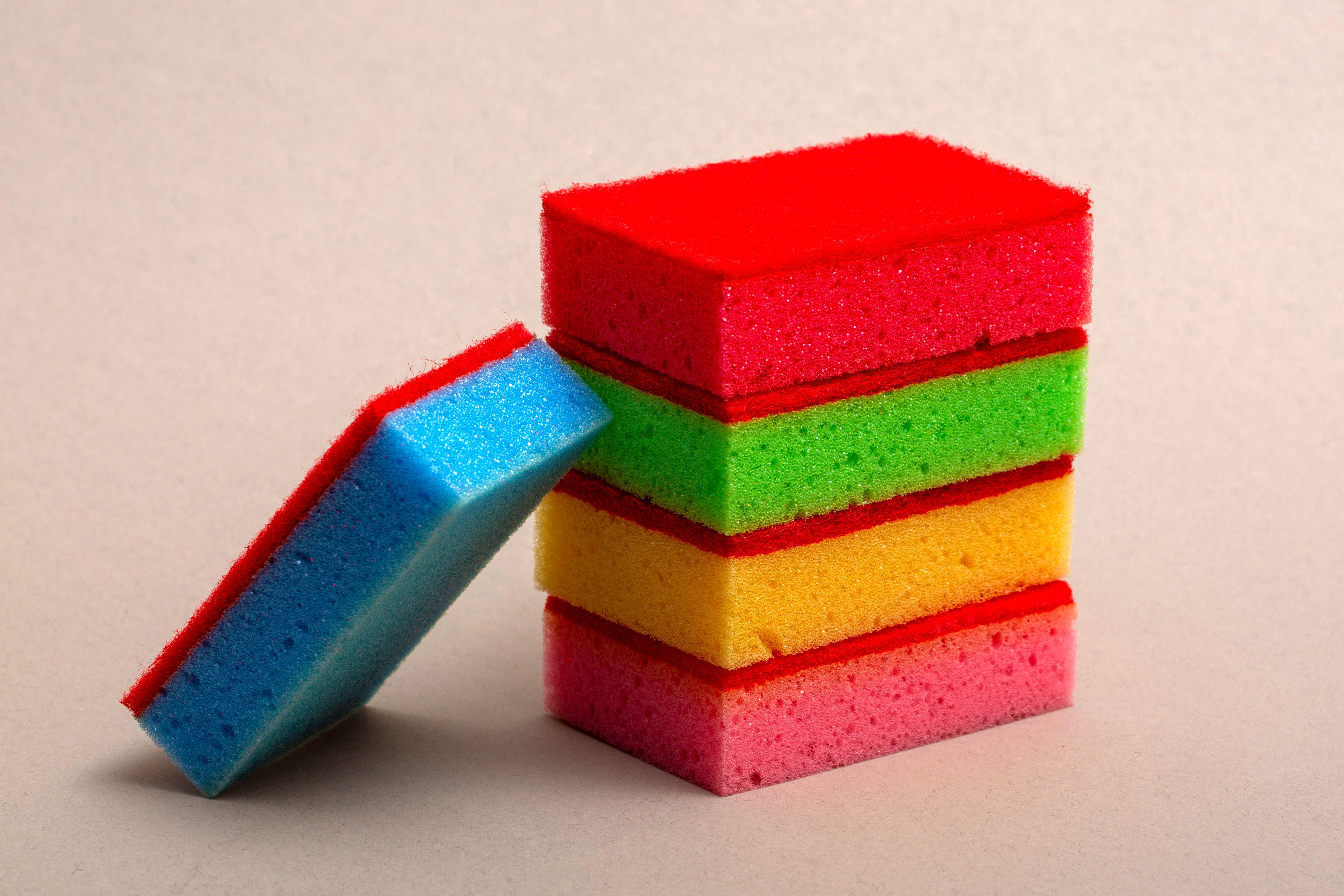 Stack of colorful kitchen sponges showing vibrant red, green, yellow, and blue hues in a studio setting.