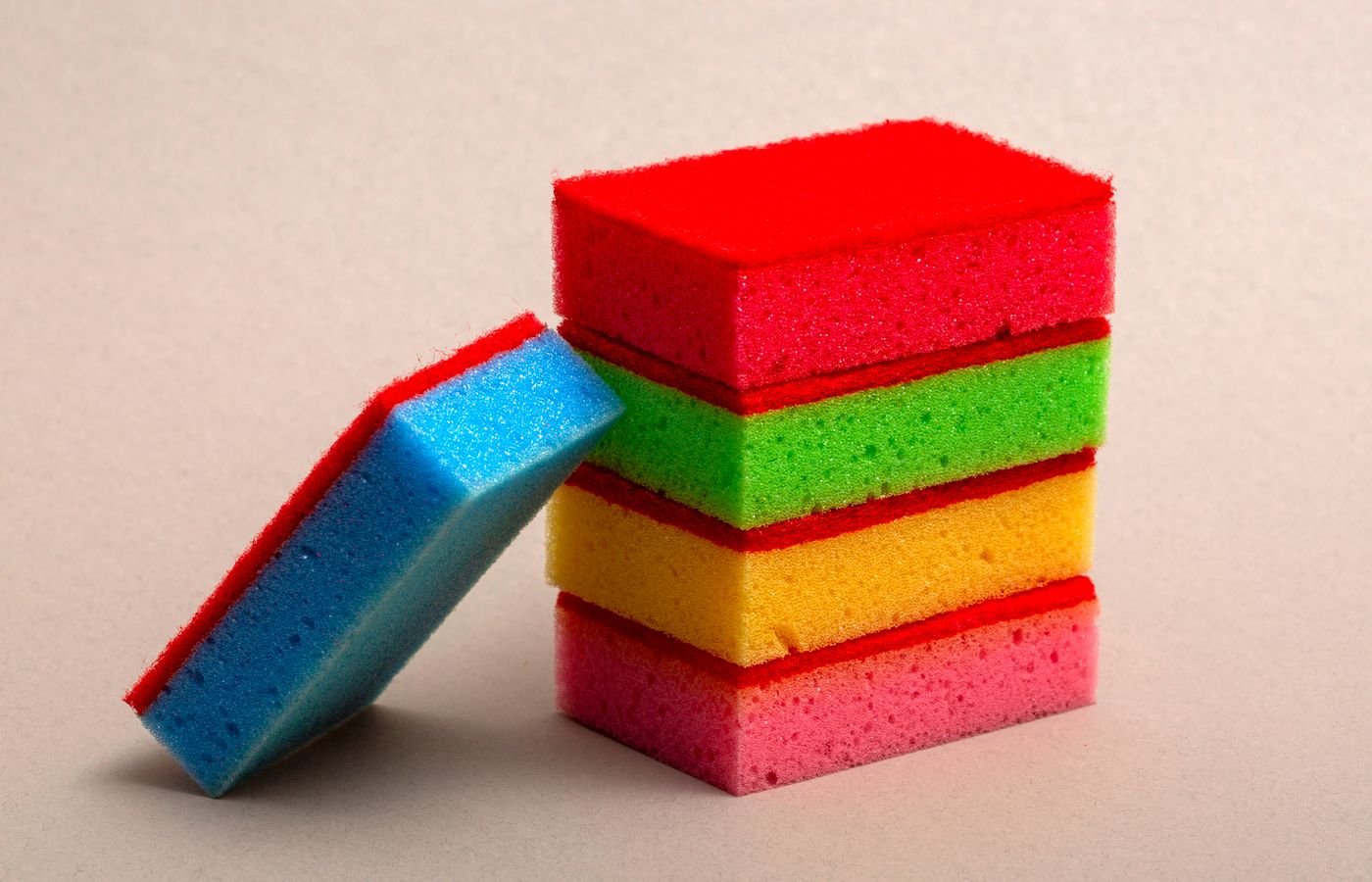Stack of colorful kitchen sponges showing vibrant red, green, yellow, and blue hues in a studio setting.