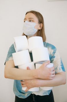 A woman wearing a face mask holds multiple toilet rolls, symbolizing pandemic hoarding.