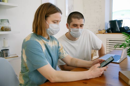 Free Woman with Face Mask Using Cellphone Beside a Man Using Laptop Stock Photo