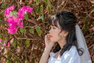 一位戴着面纱、身着白色婚纱的年轻冷静的少数族裔女性，站在开着精致花朵的树枝旁