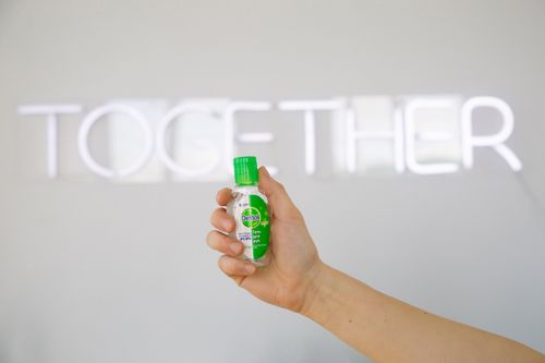 Free Close-up of hand holding sanitizer bottle against a neon sign background. Stock Photo