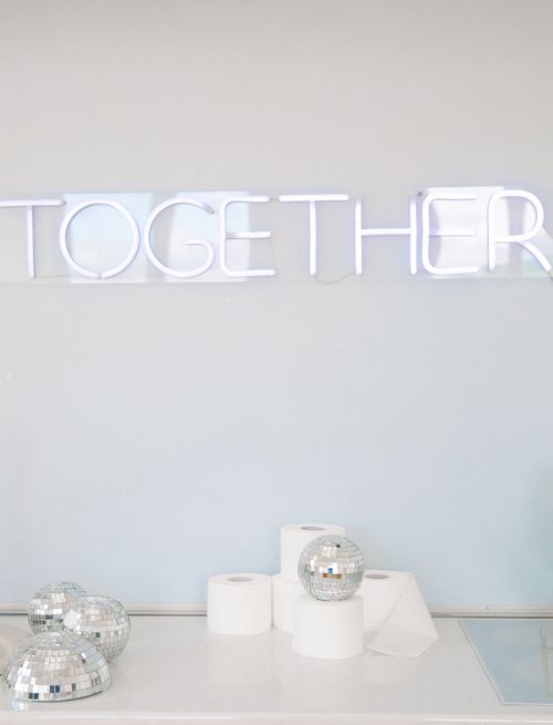 Free Minimalistic image featuring a neon 'Together' sign with disco balls and toilet paper rolls on a white surface. Stock Photo