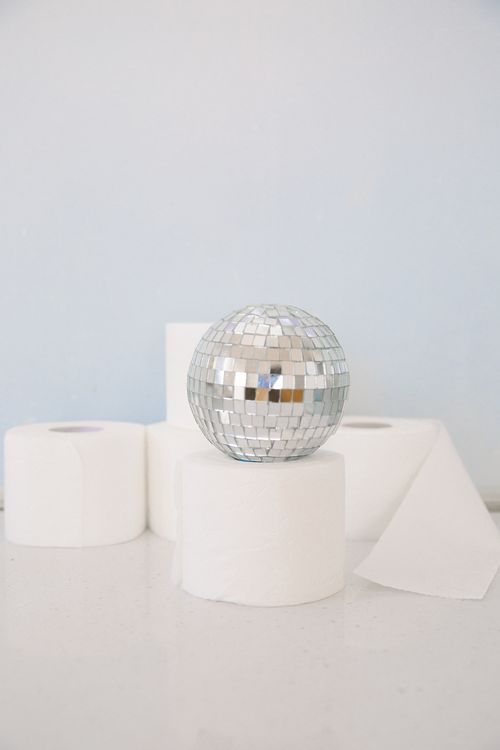 Free A playful composition featuring a silver disco ball atop rolls of toilet paper, combining humor and creativity. Stock Photo
