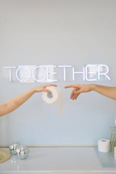 Artistic photo of hands holding toilet paper in front of a neon 'Together' sign indoors.