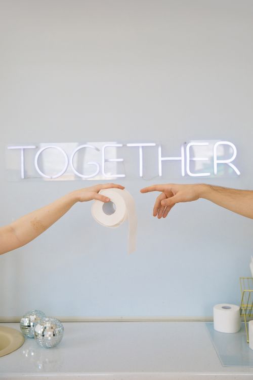 Free Artistic photo of hands holding toilet paper in front of a neon 'Together' sign indoors. Stock Photo