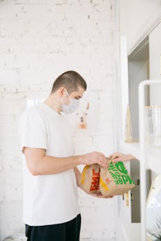 Man wearing a face mask holds paper delivery bags in a bright indoor setting.