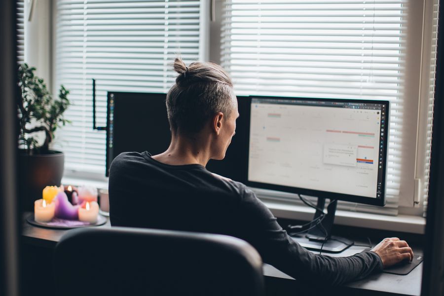Engineer working at a multi-monitor home-office desk, seen from behind. Photo by Pablo Buendia on Pexels.
