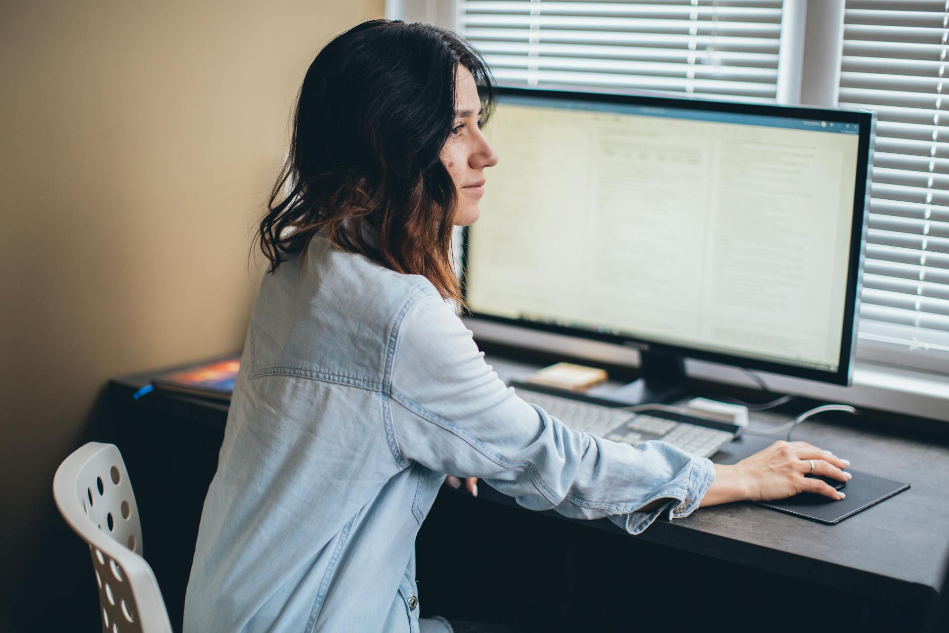 A woman working remotely from her home office desk using a computer monitor.