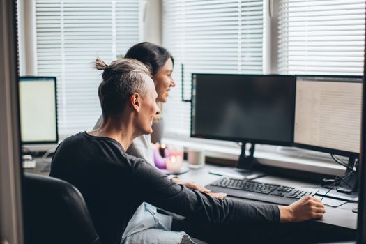 Joyful couple collaborating in a home office setting with computers and natural lighting.