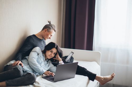 Free Happy couple working remotely on laptops in a cozy bedroom setting. Stock Photo