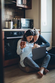 Smiling couple bonding over coffee and laptop in a cozy kitchen setting.