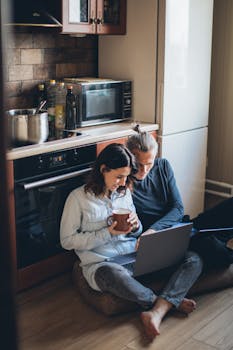 Couple sitting on the kitchen floor, sharing warm moments with a laptop and coffee.