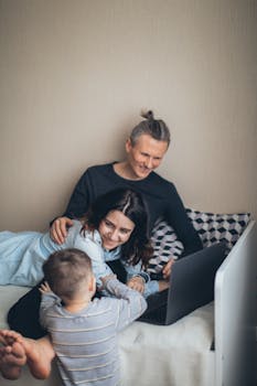 A joyful family spending quality time together on a bed while using a laptop.