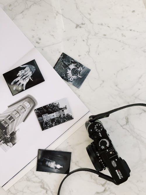 From above of photo camera arranged with black and white photos of album on marble surface