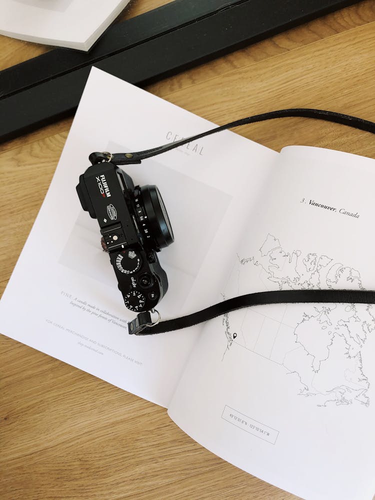 Black Photo Camera Placed On White Book On Wooden Table In Room