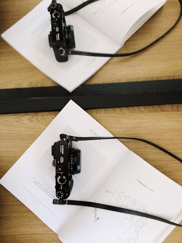 Photo Camera Placed On White Page Of Book On Wooden Table Near Mirror