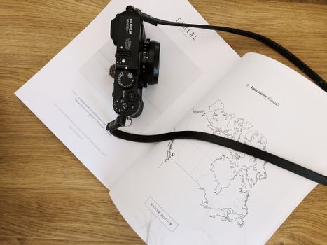 From above of photo camera placed on page of opened book on wooden table in modern studio