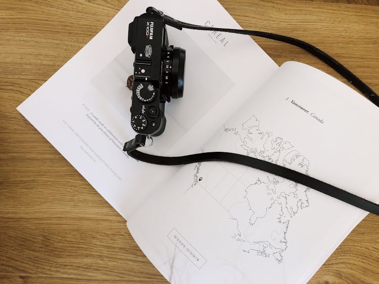 Photo Camera Placed On Page Of Opened Book On Wooden Table