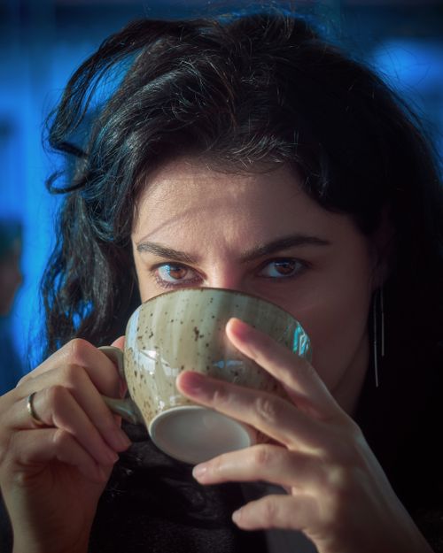 Free Close-up of a woman sipping a drink from a mug in an indoor setting with blue tones. Stock Photo