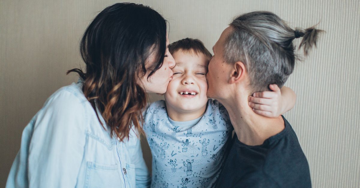 A joyful family moment with two parents kissing their smiling son indoors, symbolizing love.