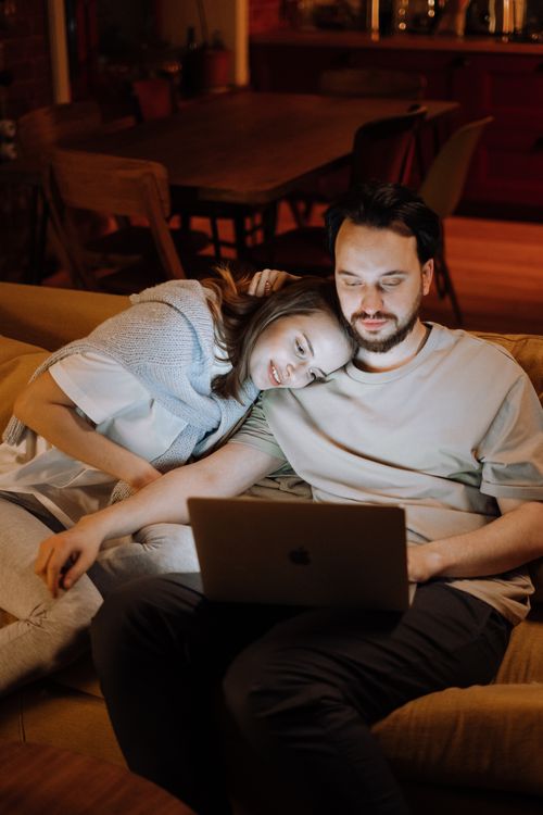 Free Couple enjoying a quiet evening on the sofa together at home, using a laptop. Stock Photo