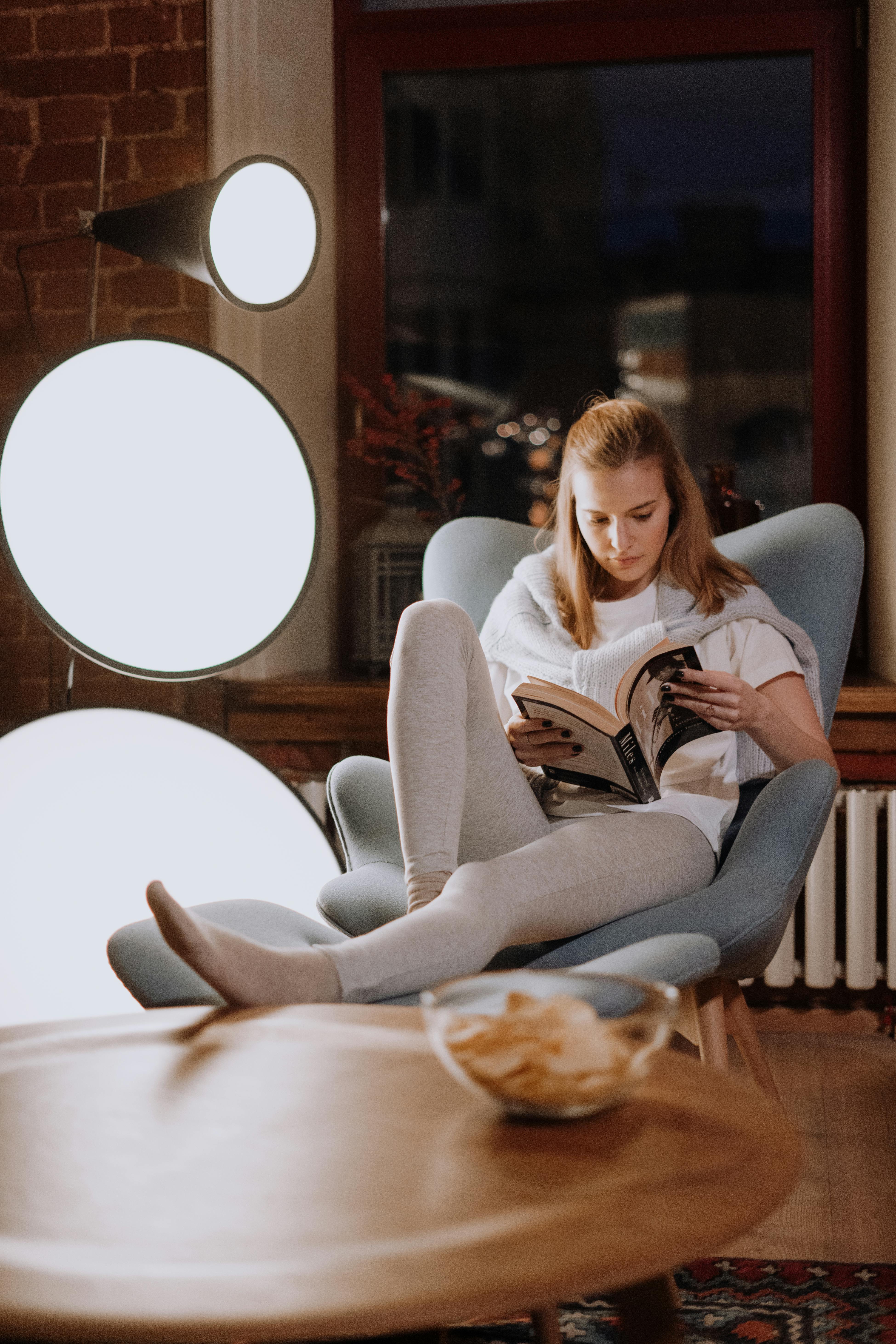 A woman relaxes and reads a book in a stylish, warmly lit living room.