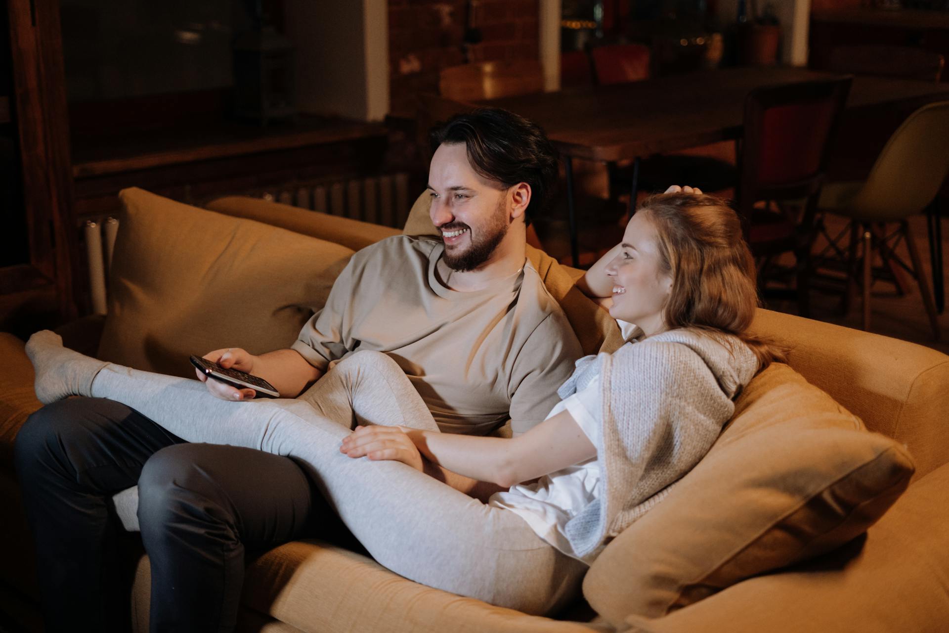 A loving couple relaxing on the sofa in a cozy home interior during the evening, enjoying a peaceful moment together.