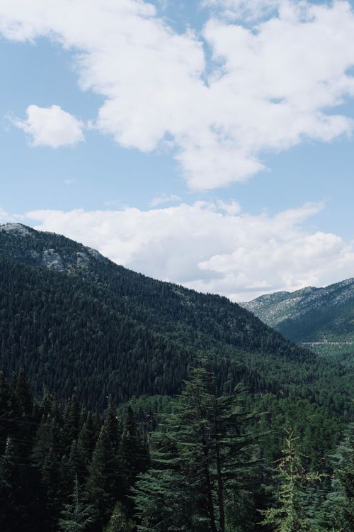 Free A scenic view of a mountain landscape with dense forest under a blue sky. Stock Photo