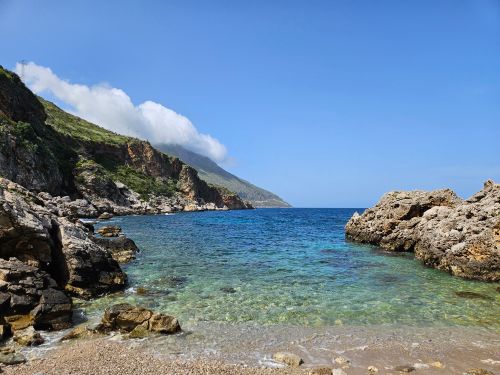 Free A captivating view of Sicily's rugged coastline with clear blue sea and rocky formations under a bright sky. Stock Photo