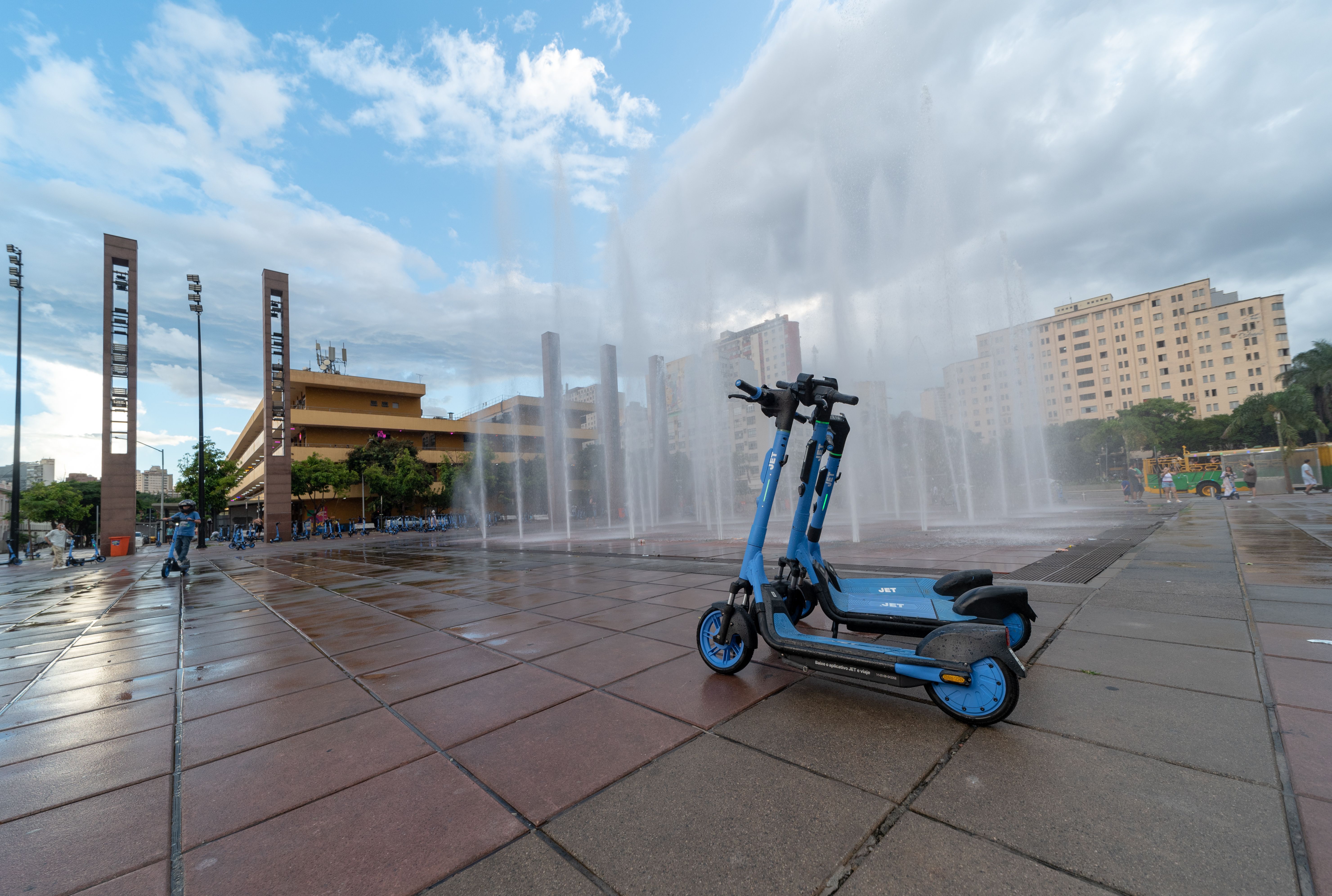 Blue scooters parked in front of fountains at a plaza in Belo Horizonte, Brazil.