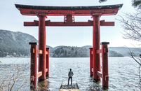 在日本的芦之湖上，一个人站在箱根神社标志性的鸟居门前，景色宁静