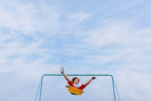 Free Young child swinging high under a clear blue sky, experiencing joy and freedom outdoors. Stock Photo