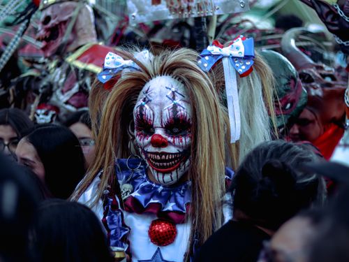 Free A creepy clown with detailed makeup and costume amidst a lively Mexican parade crowd. Stock Photo
