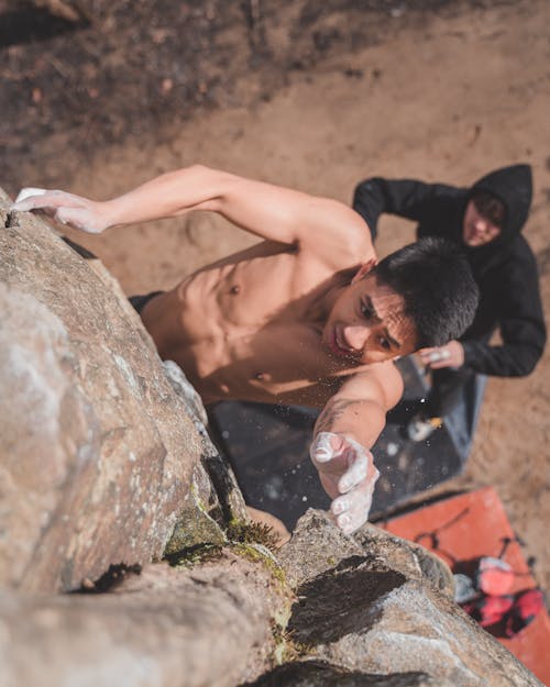 From above of shirtless young male climber falling off rocky cliff during training with partner
