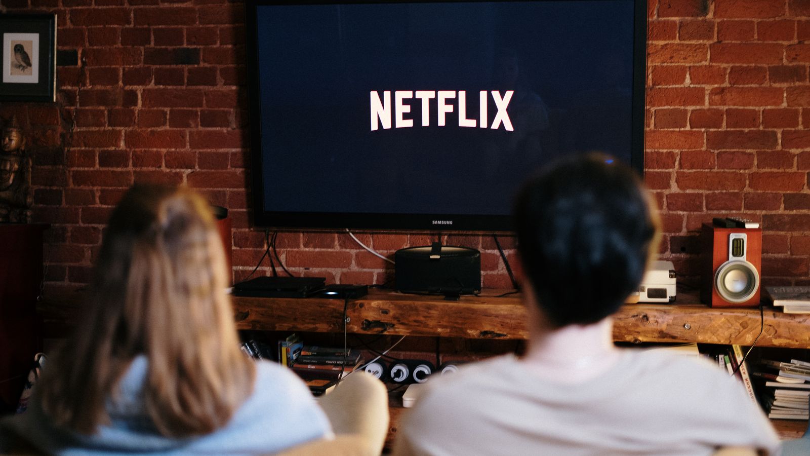 Two adults seen from behind, facing a television displaying the Netflix logo
