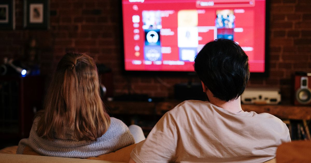 Couple sitting together on a couch watching a TV screen in a cozy brick-walled room