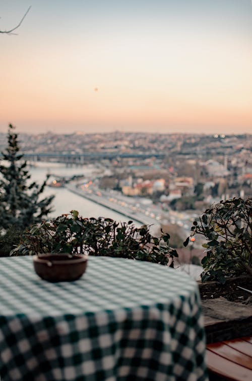 Round table covered with green checkered tablecloth in outdoor cafe with amazing city view during sunset