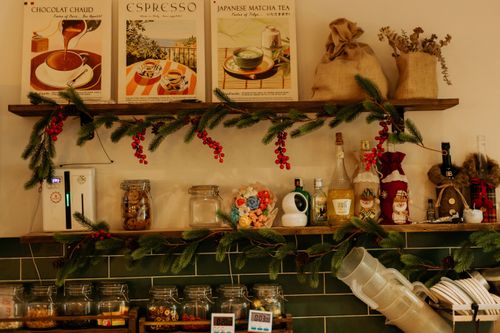 Free A warmly decorated kitchen shelf with holiday garlands, mugs, and retro drink posters, evoking a festive ambiance. Stock Photo